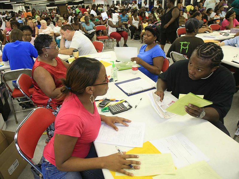 Lekita Colclough (left) with the Central Arkansas Development Council helps Anthony Waits with his application Monday at the State Fairgrounds in Little Rock during a mass intake day for the Low Income Home Energy Assistance Program. The program helps low-income households pay their electric bills. 