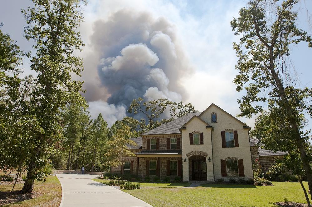 Wildfire smoke billows behind a home in the Crown Ranch subdivision near Montgomery, Texas on Tuesday, Sept. 6, 2011. More than 1,000 homes have been destroyed in at least 57 wildfires across rain-starved Texas, most of them in one devastating blaze near Austin that is still raging out of control, officials said Tuesday. (AP Photo/The Courier, Karl Anderson)