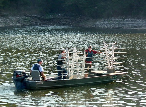 Ron Moore and John Stein, fisheries biologists for the Arkansas Game and Fish Commission, and conservation technician Jacob Shipman launched a boat filled with fake trees to be submerged in Crystal Lake for fish habitat on Thursday morning.