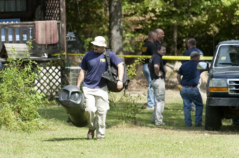 An FBI agent hauls gear away from a Traskwood home where authorities found two sets of human remains Wednesday. 
