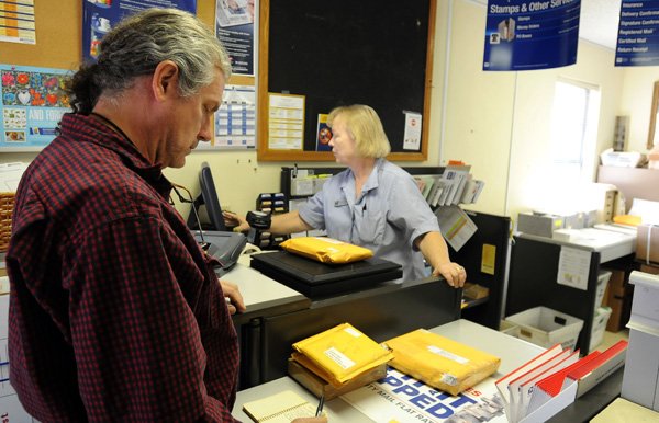 Jean Helmer, sales associate at the Johnson Post Office, right, helps Kim Foster on Friday in Johnson. Foster said he uses Johnson’s Post Office about three times a week and doesn’t think closing it is in the best interest of Johnson or the Postal Service. Friday was the last day the office was open. All post office box service will be moved to the Fayetteville Post Office on Joyce Boulevard.
