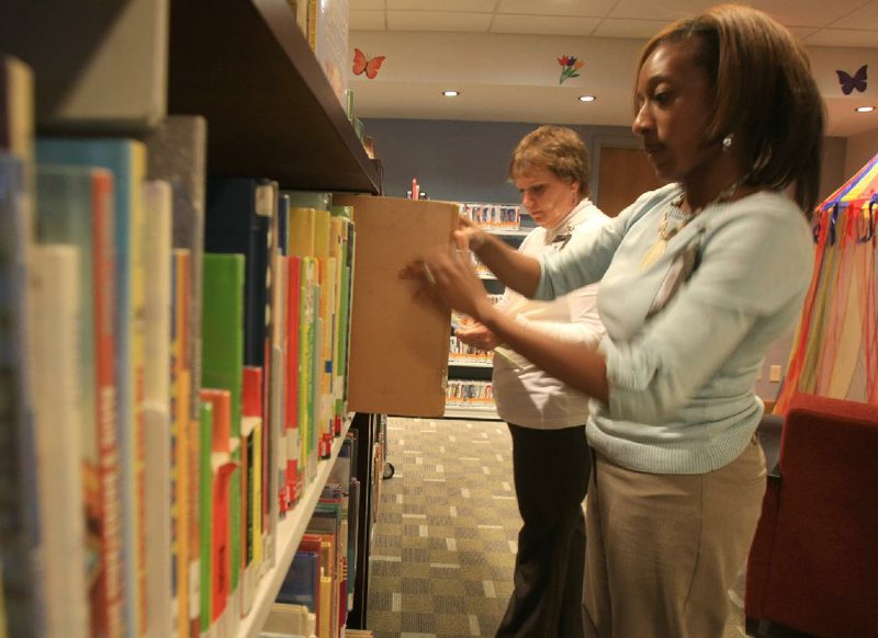 Library branch manager Kathy Sarna (left) and library assistant Autumn Thomas sort books in the small children’s area of Laman Library’s Argenta branch in North Little Rock. The downtown post office building could be the new location for the library if a proposed tax increase passes next month. 