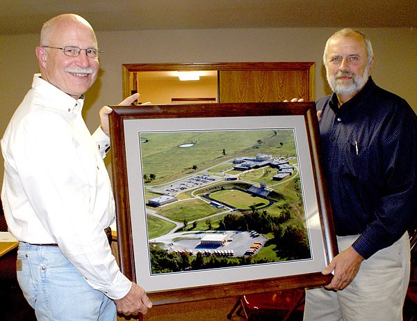 Marion Harris, right, was presented a framed photo of the new Gravette High School campus, projects completed during his tenure on the board. Making the presentation during a meeting of the school board last week was Dan Yates, new school board president.
