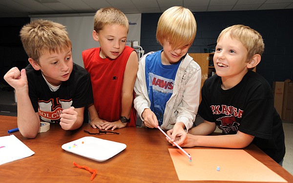 Cameron Boyd, from left, Collin Schultz, Keaton Moreland and Charlie Faught, all Holcomb Elementary School fourth-graders, laugh Wednesday as they try to win a timed competition and move a collection of beads with a device they made from a pipe cleaner and a soda straw during an after school science club meeting at the Fayetteville school.
