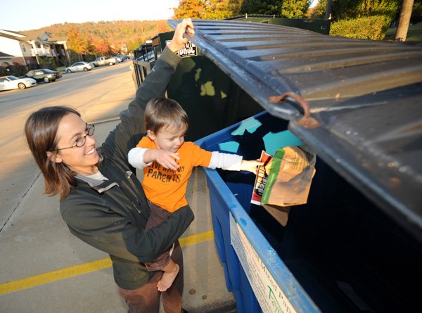 Stephanie Kellner, left, holds 2-year-old son August so he can deposit paper into a recycling container Tuesday at The Cliffs in east Fayetteville. The city is launching a program that will allow residents of apartments to recycle using containers rotated between two area complexes. “I saw this yesterday and I was so happy,” said Kellner.
