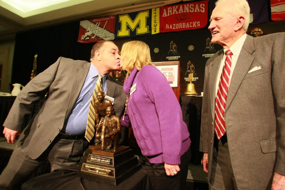 Arkansas Democrat-Gazette/RICK MCFARLAND --12/06/11-- John Chavis, Louisiana State University defensive coordinator, kisses his wife Diane over the Broyles Award trophy after he was named Tuesday in Little Rock as the 16th recipient of the award, given annually to the top assistant coach in college football. Frank Broyles (right), former Arkansas Coach and Athletic Director, for whom the award was named was there to present it.