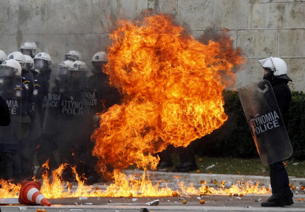 A petrol bomb explodes in front of riot police officers guarding the Tomb of the Unknown Soldier in front of the Parliament during a protest in Athens, Tuesday, Dec. 6, 2011. Protesting high school students hurled rocks and bottles during clashes clashed with police Tuesday during a rally to mark the third anniversary of the fatal police shooting of a teenager in central Athens. (AP Photo/Kostas Tsironis)