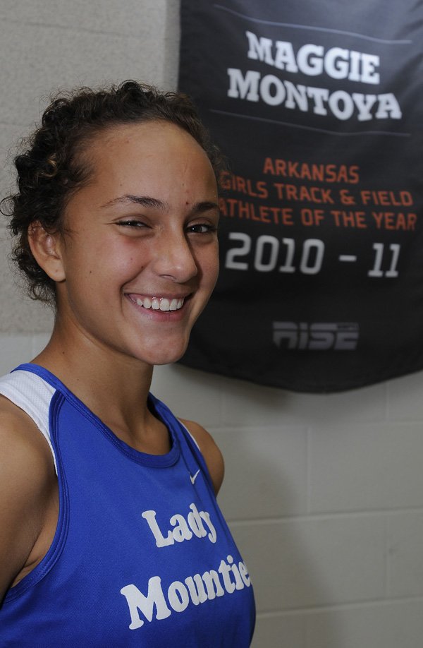 Maggie Montoya smiles Dec. 9 while standing in front of the banner that names her the Gatorade Arkansas Girls Track and Field Athlete of the Year at the Rogers High School fieldhouse.