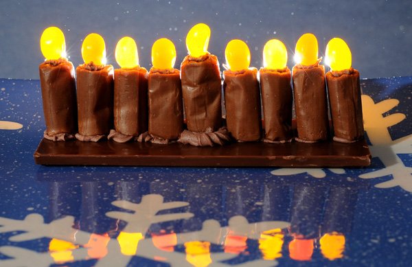 Creating an edible menorah requires chocolate frosting, Tootsie Rolls and orange and yellow jelly beans.