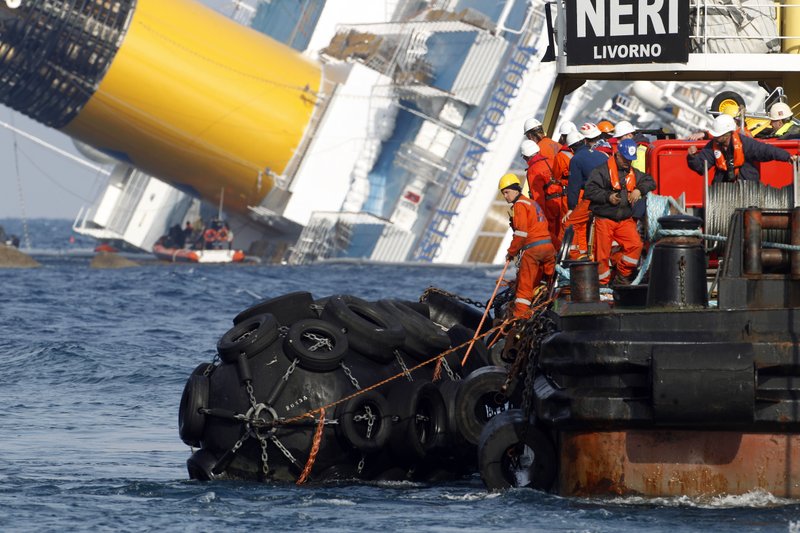 Experts aboard a sea platform carry oil recovery equipment as they return to the port of the Tuscan island of Giglio, Italy, where the cruise ship Costa Concordia, visible in background, ran aground, Saturday, Jan. 28, 2012. Rough seas off Italy's Tuscan coast forced a delay in the planned Saturday start of the operation to remove a half-million gallons of fuel from the grounded Costa Concordia, and officials said pumping may now not begin until midweek.