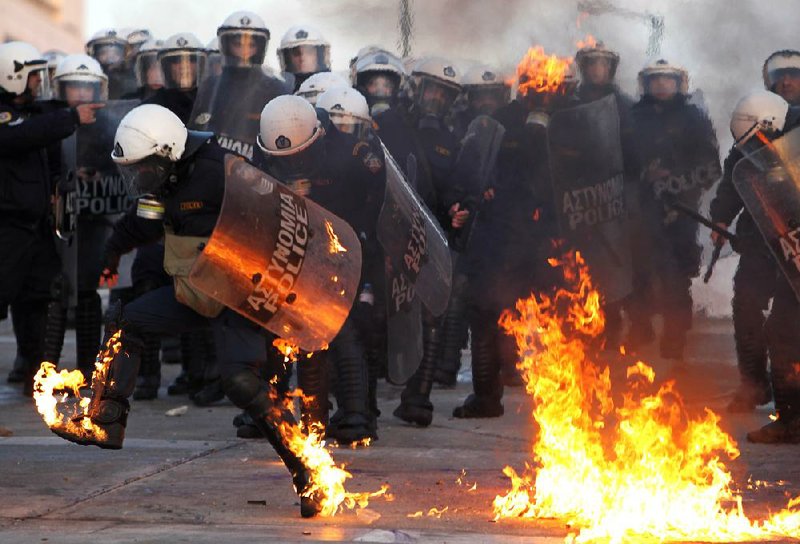 A riot police officer tries to extinguish flames from a gasoline bomb thrown Sunday by protesters outside the Greek Parliament in Athens. 