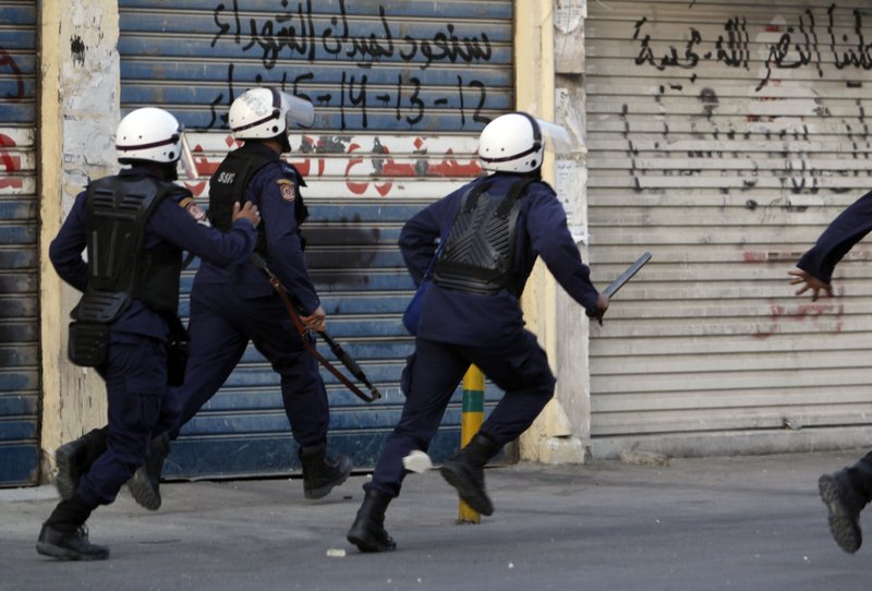 Riot police chase anti-government protesters, unseen, in Sanabis, Bahrain, on the edge of the capital of Manama on Sunday, Feb. 12, 2012, as protesters' attempts were thwarted to head toward an area nearby they call "Martyrs Square" that had served as the main hub for last spring's pro-democracy uprising. Writing on the garage door reads: "We will return to Martyrs Square 12-13-14-15 February." 