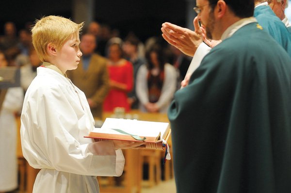 Grayson Laman, altar server at St. Vincent de Paul Catholic Church in Rogers, holds the Roman Catholic Missal on Feb. 5 as Monsignor David LeSieur, with hands up, reads from the book during Mass. Church members are adapting to missal changes mandated by the Roman Catholic church last year.
