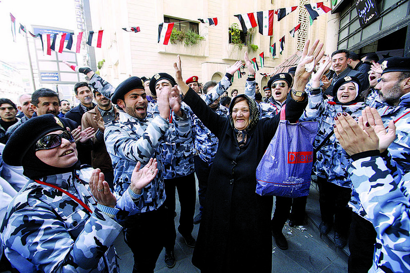 A Syrian woman dances with pro-Syrian regime supporters in police uniforms as they celebrate outside a polling station during a referendum on a new constitution in Damascus on Sunday. 