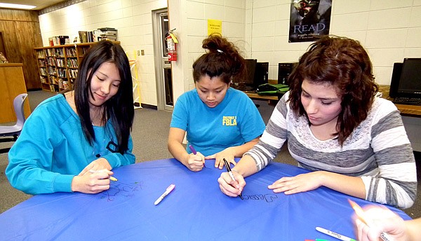 Kaula Yang, Youa Vang and Jessica Segovia signed a tablecloth for the bake sale booth. The fundraising bake sale will be held today at the Northwest Arkansas Community College to raise money to help Decatur students pay for ACT testing fees.
