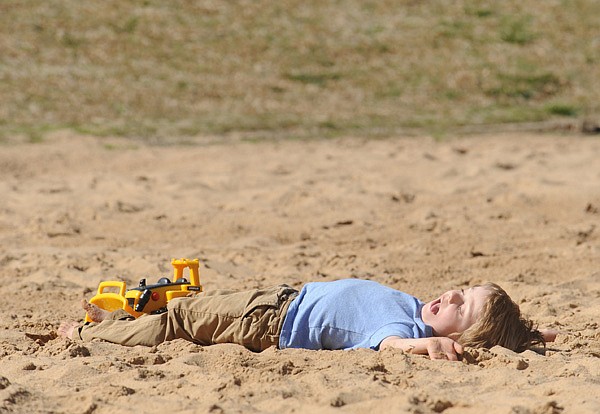 Owen Dixon, 4, of Fayetteville smiles as he takes a moment to lie in the sun Wednesday while playing with friend Andrew Simmons in the volleyball pit at Gulley Park in Fayetteville.