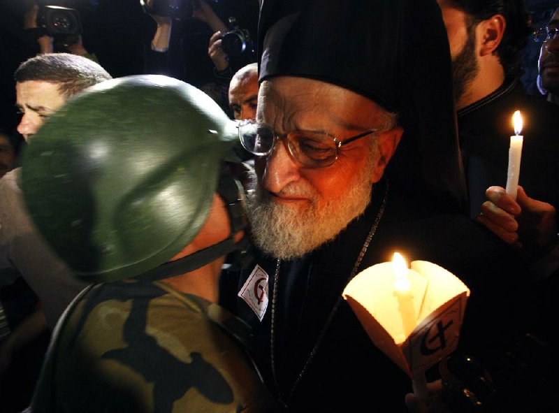 A Syrian army soldier, left, kisses Gregarious Laham, Patriarch of Antioch and the whole East for the Romans Catholics, right, during a candlelight vigil after a mass prayer for the civilian citizens and security officers who were killed during the last two explosions that attacked Syrian security departments last Saturday, in Damascus, Syria, on Wednesday March 21, 2012. The previously divided U.N. Security Council sent a strong and united message to the Syrian government and opposition on Wednesday to immediately implement proposals by international envoy Kofi Annan to end the yearlong bloodshed. (AP Photo/Muzaffar Salman)