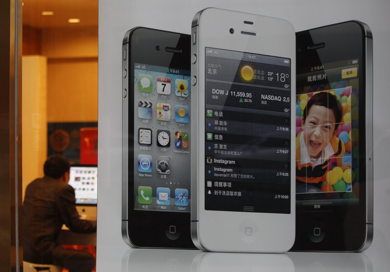 An employee surfs Internet behind an iPhone poster at a phone shop in Beijing Saturday, April 7, 2012. Authorities indicted five people in central China for involvement in illegal organ trading after a teenager sold one of his kidneys to buy an iPhone and an iPad. 