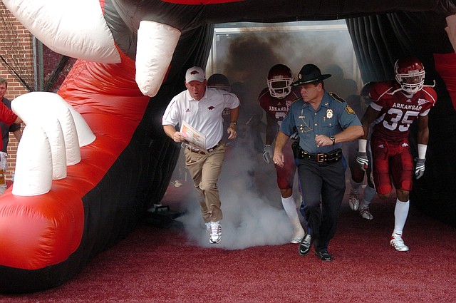 FILE - Bobby Petrino (left) and Capt. Lance King with the Arkansas State Police (right) run with the Razorbacks onto the field at Reynolds Razorback Stadium in Fayetteville.