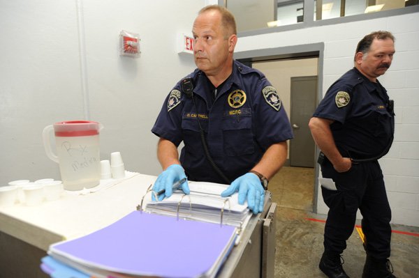 Doug Cantrell, left, and John E. Byrd, detention officers at the Washington County Dentention Center in Fayetteville, dispense prescribed medication Friday to detainees at the facility and log the information. 