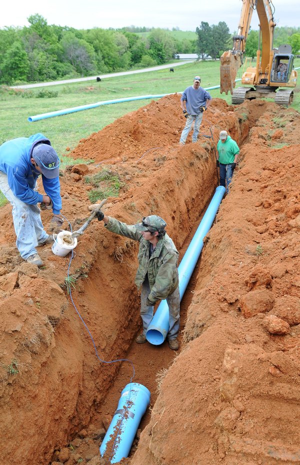 Shane Yeakley, top center, and Scott Seaman, right, watch as Mario Trecanao, left, holds a bucket of pipe lubricant for Dustin Sams, bottom center, as the crew installs water pipe lines. 