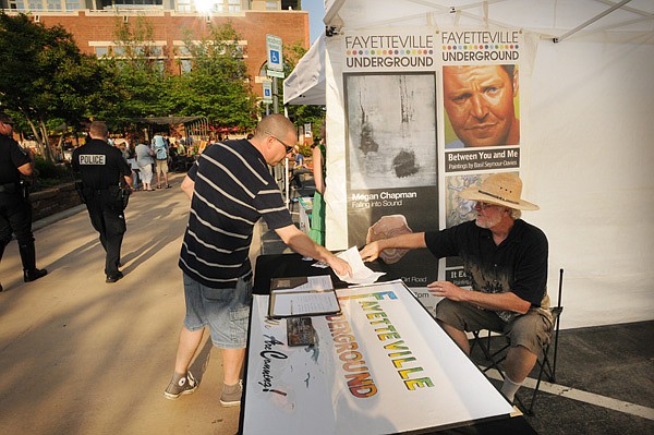 Mathew Jay, left, looks over floor plans Thursday for a new location for the Fayetteville Underground with MM Kent at the Underground’s booth during the First Thursday event on the Fayetteville square. The Underground is requesting $60,000 from the Fayetteville Advertising and Promotion Commission and is looking to move into the GCM Building at the corner of Mountain Street and Block Avenue.