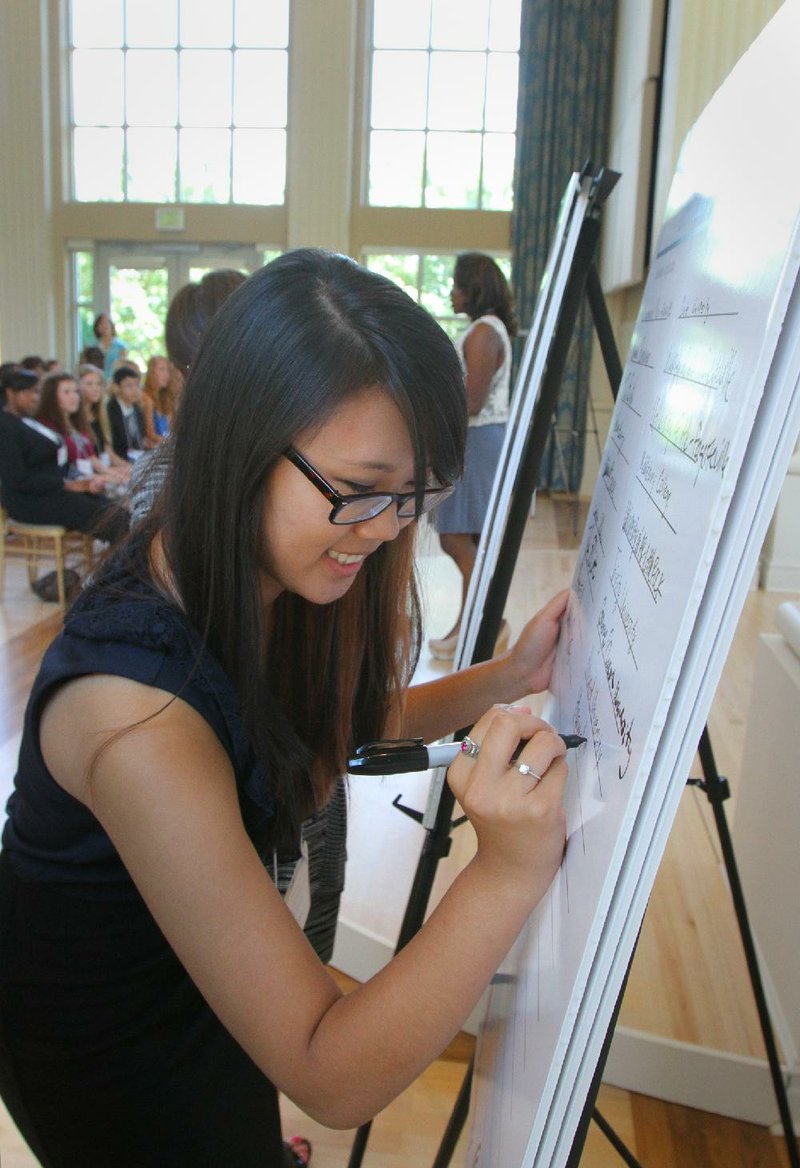 Little Rock Central High School senior Whitney Gao signs her name and college choice on a board at an event recognizing top scholars Monday at the Governor’s Mansion in Little Rock. 