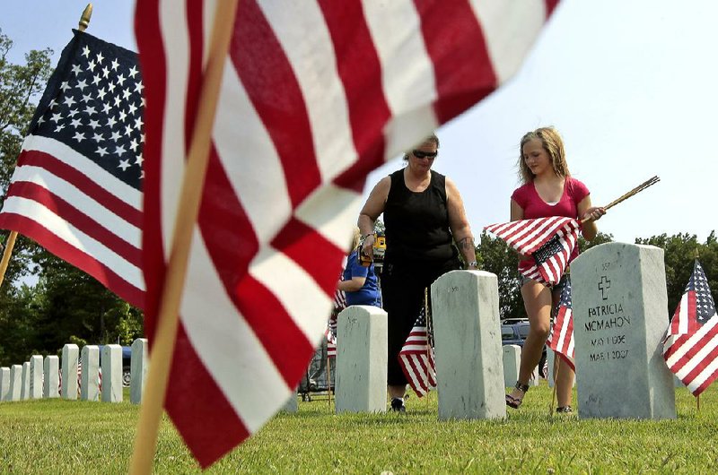 Donna Johnson, Lacey Finch and other volunteers place flags Thursday by the 4,800 headstones at the Arkansas State Veterans Cemetery in North Little Rock in preparation for Memorial Day ceremonies. 