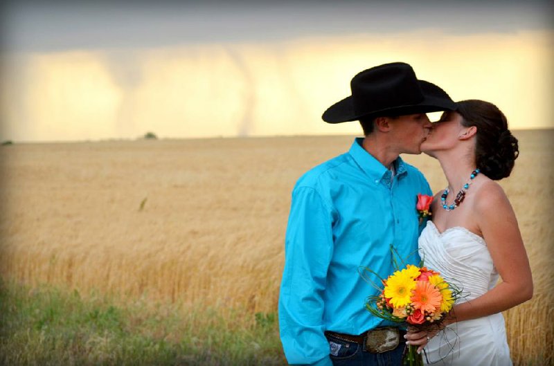 Caleb and Candra Pence pose for a wedding photo as a tornado swirls in the background after they were married Saturday in Harper County, Kan. 