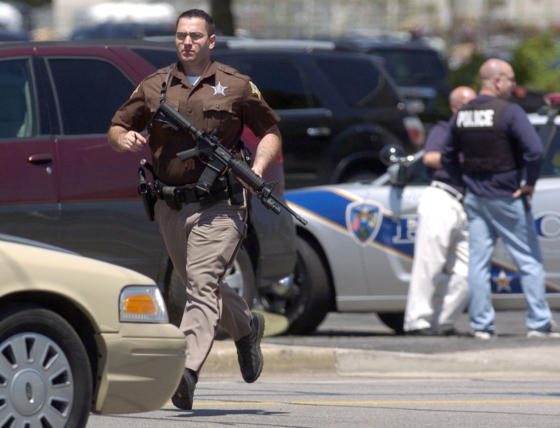 A Porter County sheriff's officer runs as Valparaiso police officers take cover behind a squad car during a standoff at a real estate office Friday, May 25, 2012, in Valparaiso, Ind. 