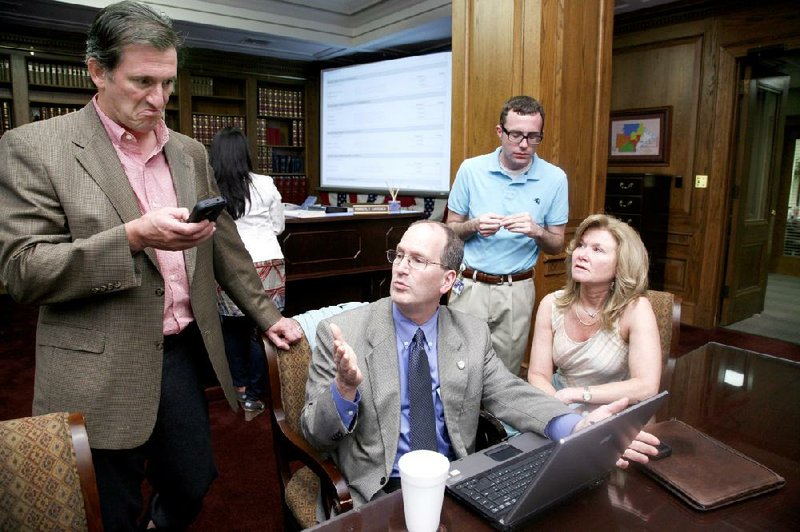 Bill Murphy (left), with ENR software, checks his smart phone as A.J. Kelly (second from left), Alex Reed and Cynthia Fisher, all with the secretary of state’s office, discuss election-night results Tuesday. 
