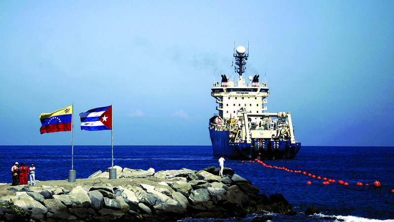 People stand on a breakwater next to Venezuelan (left) and Cuban flags as a ship rolls out a fiber-optic cable suspended from buoys on the Venezuelan coast in this file photo. 