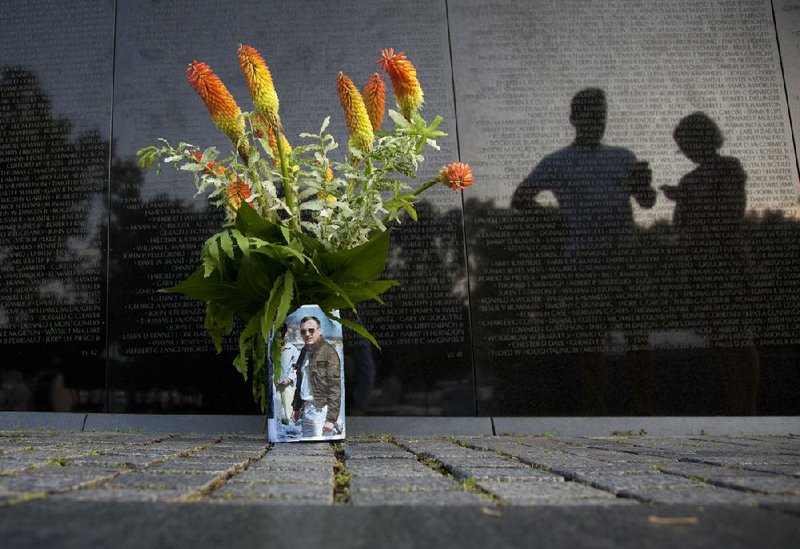 A bouquet of flowers with a photo is seen as visitors pause to view the Vietnam Veterans Memorial Wall on Monday in Washington. 