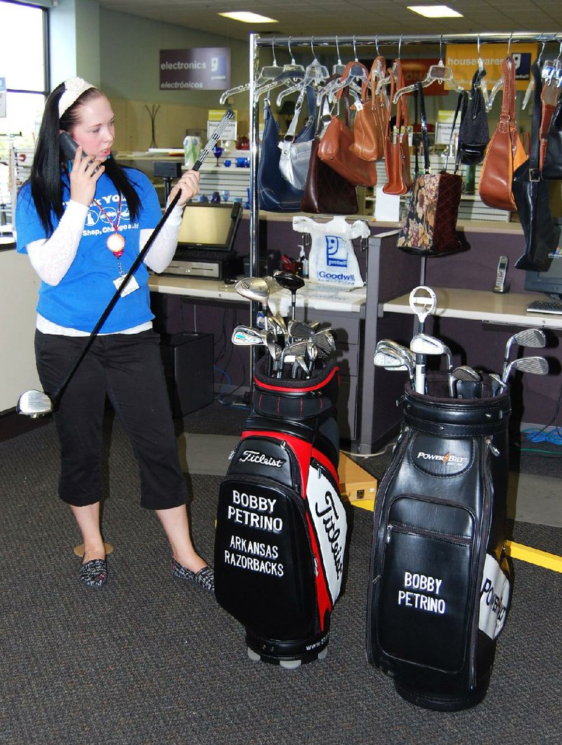 Mercedes Moseley, an employee at the Goodwill store in Springdale, examines golf clubs that had belonged to Bobby Petrino. 