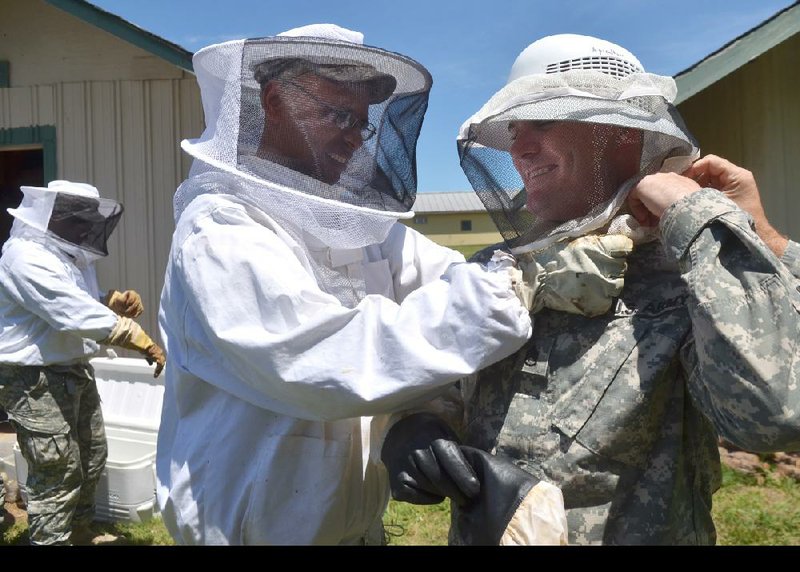 1st Sgt. John Paxton of Memphis (left) helps Staff Sgt. Carl Addis of Little Rock get into beekeeping gear Tuesday as they and other members of the Army Reserve 431st Civil Affairs Battalion prepare to get a closer look at bee hives at the University of Arkansas at Fayetteville.