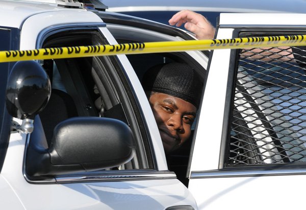 An unidentified, handcuffed man smiles from the back of Fayetteville police vehicle Thursday at 1233 N. Boxley Ave. where officers were called for a report of a shooting. The event led to one person being taken to Washington Regional Medical Center with injuries. Several people are being questioned by police. 