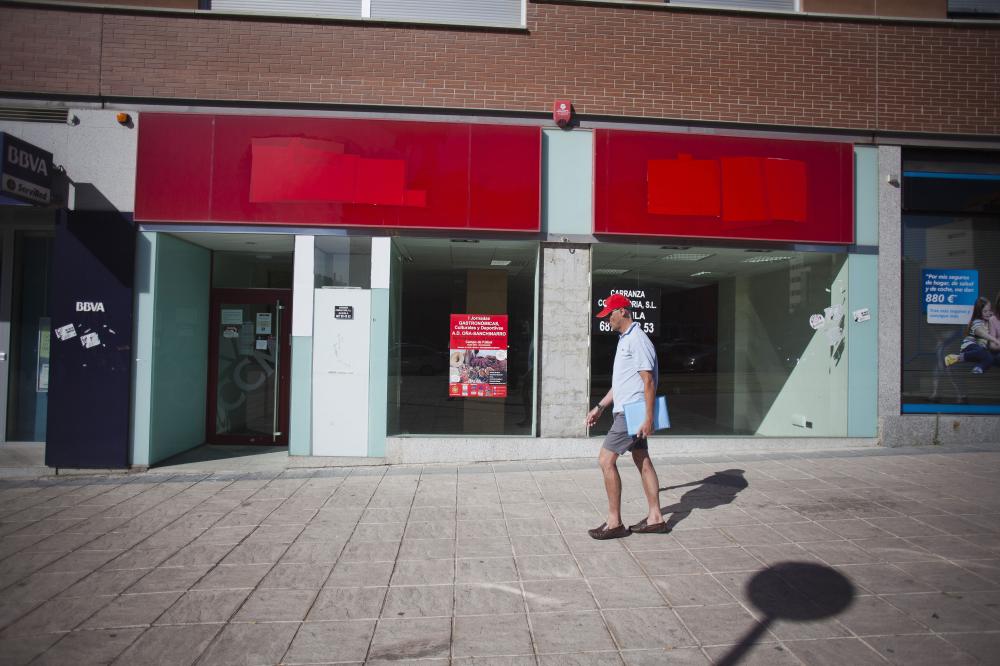 A pedestrian passes a former Caja Castilla-La Mancha bank branch with the bank's logos covered on the building in Madrid, Spain, on Saturday, June 23, 2012. Banks will need a 