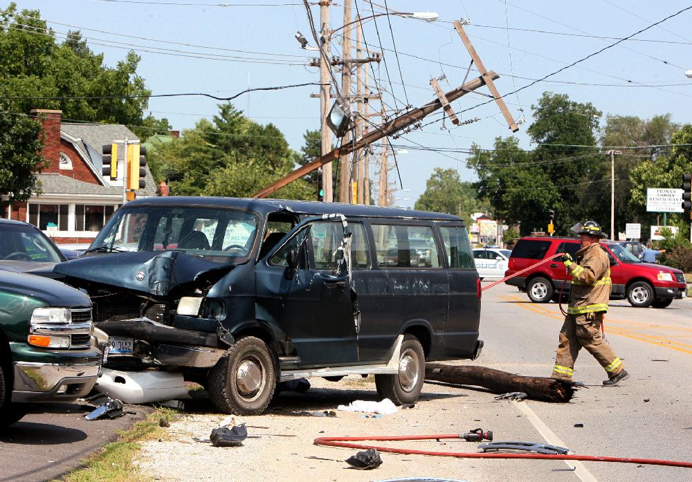 A Wood River, Ill., firefighter rolls up hoses to a hydraulic rescue tool near a van that struck and broke a utility pole, rear, on Edwardsville Road east of 6th Street in Wood River, Ill., on Monday June 25, 2012. A man driving a full-size Dodge Ram 3500 van apparently suffered a medical problem and struck the pole, breaking it in two. The van continued on and hit or damaged eight cars on the lot of Midwest Wholesale Motors. (AP Photo/The Telegraph, John Badman) THE NEWS-DEMOCRAT AND THE POST-DISPATCH OUT