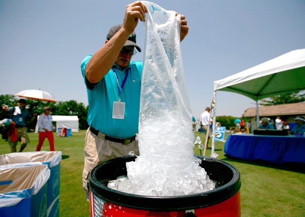 Volunteer Bob Agnew of Bella Vista dumps a bag of ice into a cooler Monday on the driving range at Pinnacle Country Club in Rogers. Professional golfers arrived in Northwest Arkansas just in time for the first predicted triple-digit temperatures of the summer.