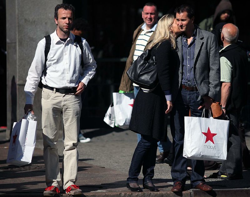 Macy’s shoppers carry their purchases outside a Macy’s store in New York in May. Consumer spending dropped less than 0.1 percent in May, the Commerce Department said Friday. 