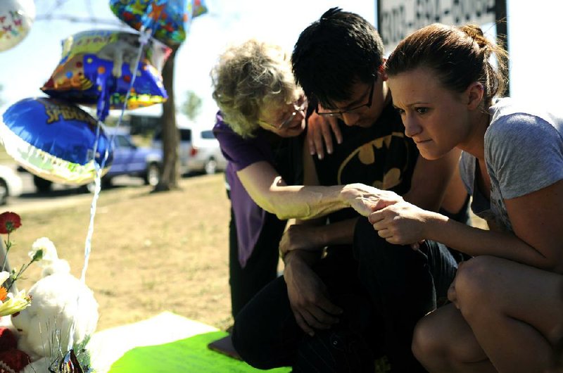 Pastor Mary Lu Saddoris (from left) comforts Isaac Pacheco and Courtney McGregor, friends of Alex Sullivan, at a memorial set up for Sullivan near the Aurora, Colo., theater where he was fatally shot. 