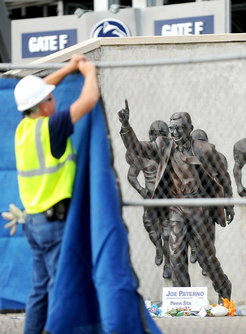 A worker hangs a tarp over the fence installed around the statue of Joe Paterno as crews work to remove the statue Sunday. 