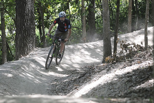 Seth Jacobs with Phat Tire Bike Shop in Bentonville rides a section of the new downhill trail Thursday at Slaughter Pen Hollow Multi-Use Trail System in Bentonville. Workers with Progressive Trail Design are finishing the new section that is supposed to be completed in August.