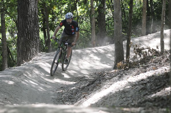 Seth Jacobs with Phat Tire Bike Shop in Bentonville rides a section of the new downhill trail Thursday at Slaughter Pen Hollow Multi-Use Trail System in Bentonville. Workers with Progressive Trail Design are finishing the new section that is supposed to be completed in August.