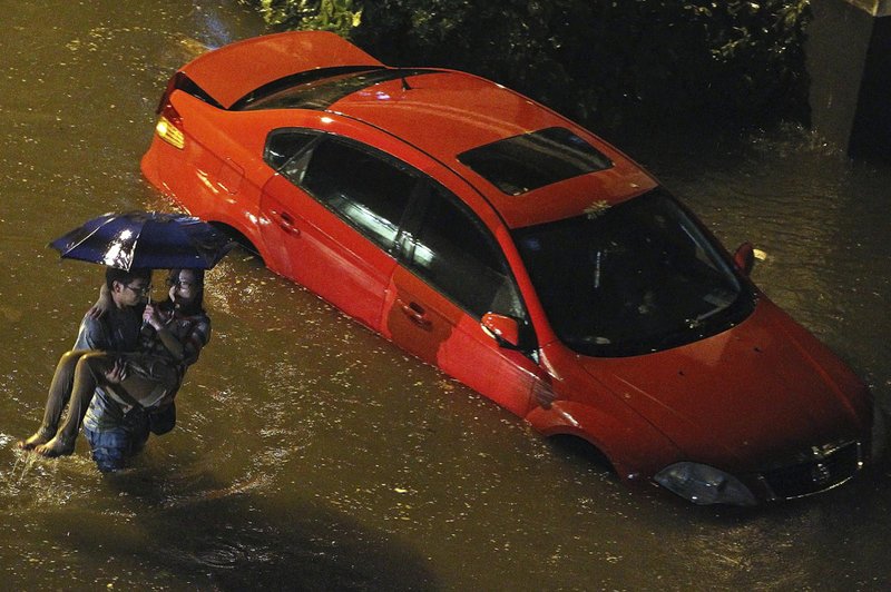 A man carries a woman past a partially submerged car in floodwaters after a heavy rain in Beijing on Saturday. 