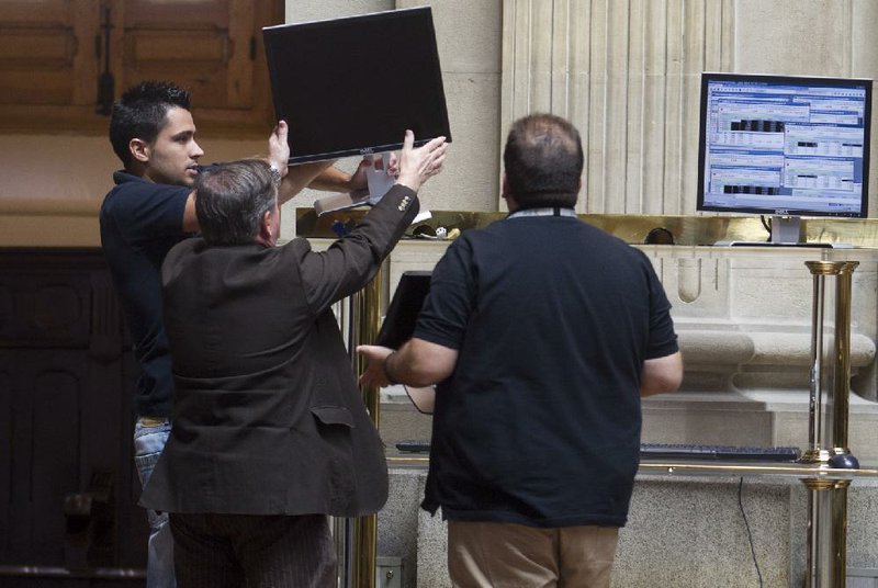 Workers try to get a screen working at the stock exchange in Madrid on Monday. The Bank of Spain says the country’s recession-plagued economy contracted 0.4 percent in the second quarter, a performance even worse than in the first three months of the year. 