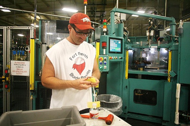 At the Baldor Electric Co. plant last week in Fort Smith, employee Michael Caple prepares insulation that’s used between copper wires in engines. Although robots are in use at the plant, people still perform most tasks. 