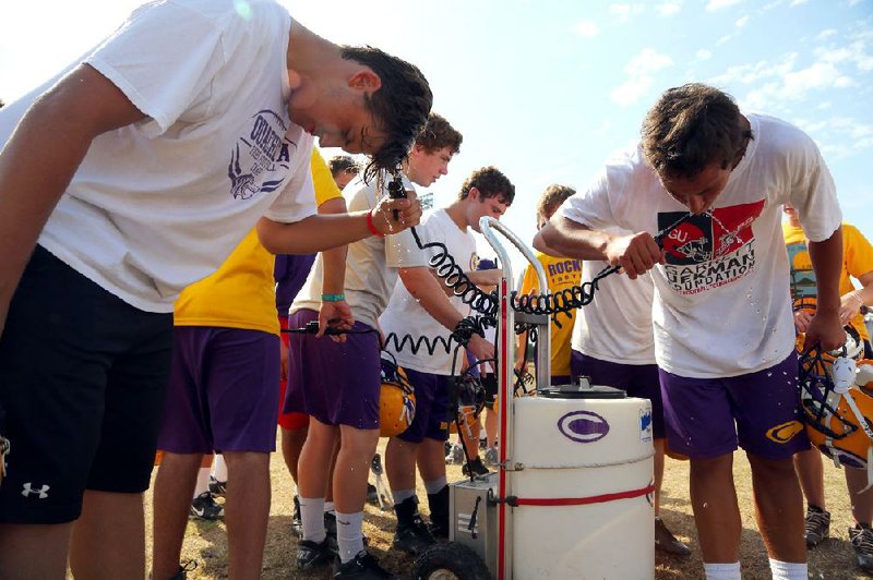 Little Rock Catholic football players take a water break during practice Monday in Little Rock. With temperatures rising above 100 degrees this summer, high school coaches are being very cautious, especially in light of new Arkansas Activities Association regulations requiring an acclimation period. 