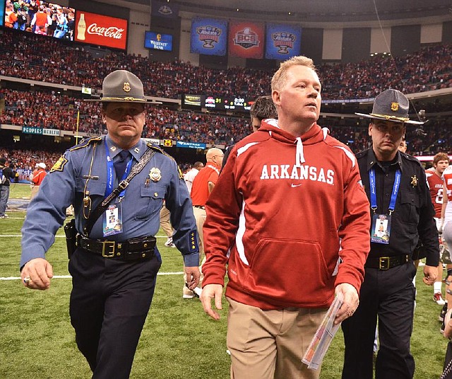 Former University of Arkansas Coach Bobby Petrino leaves the field escorted by Capt. Lance King of the Arkansas State Police after the 2011 Allstate Sugar Bowl in New Orleans. The state police agency is setting a strict policy for troopers who provide security at athletic events. 