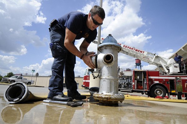 Rob Sampier, a Rogers firefighter and paramedic, caps a fire hydrant July 25 in front of Fire Station No. 1 following a training drill in downtown Rogers. 